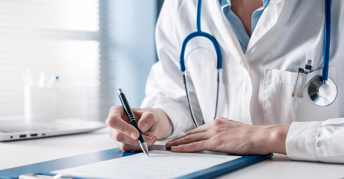 Image of a person wearing a doctor's lab coat writing something on a piece of paper