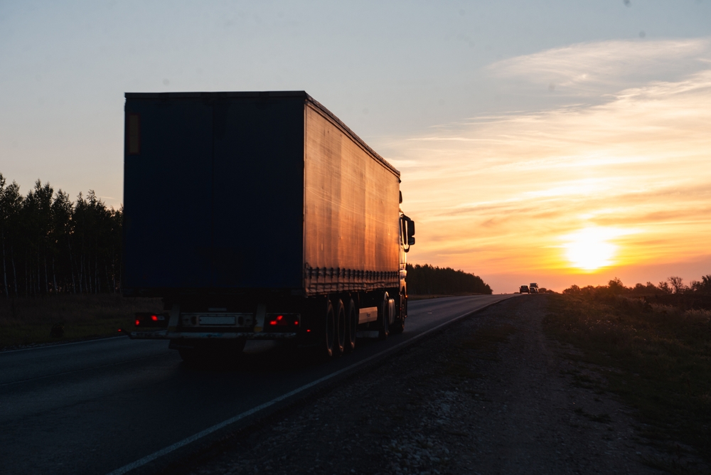 A truck drives down a highway at sunset, symbolizing road user charging for fleets.